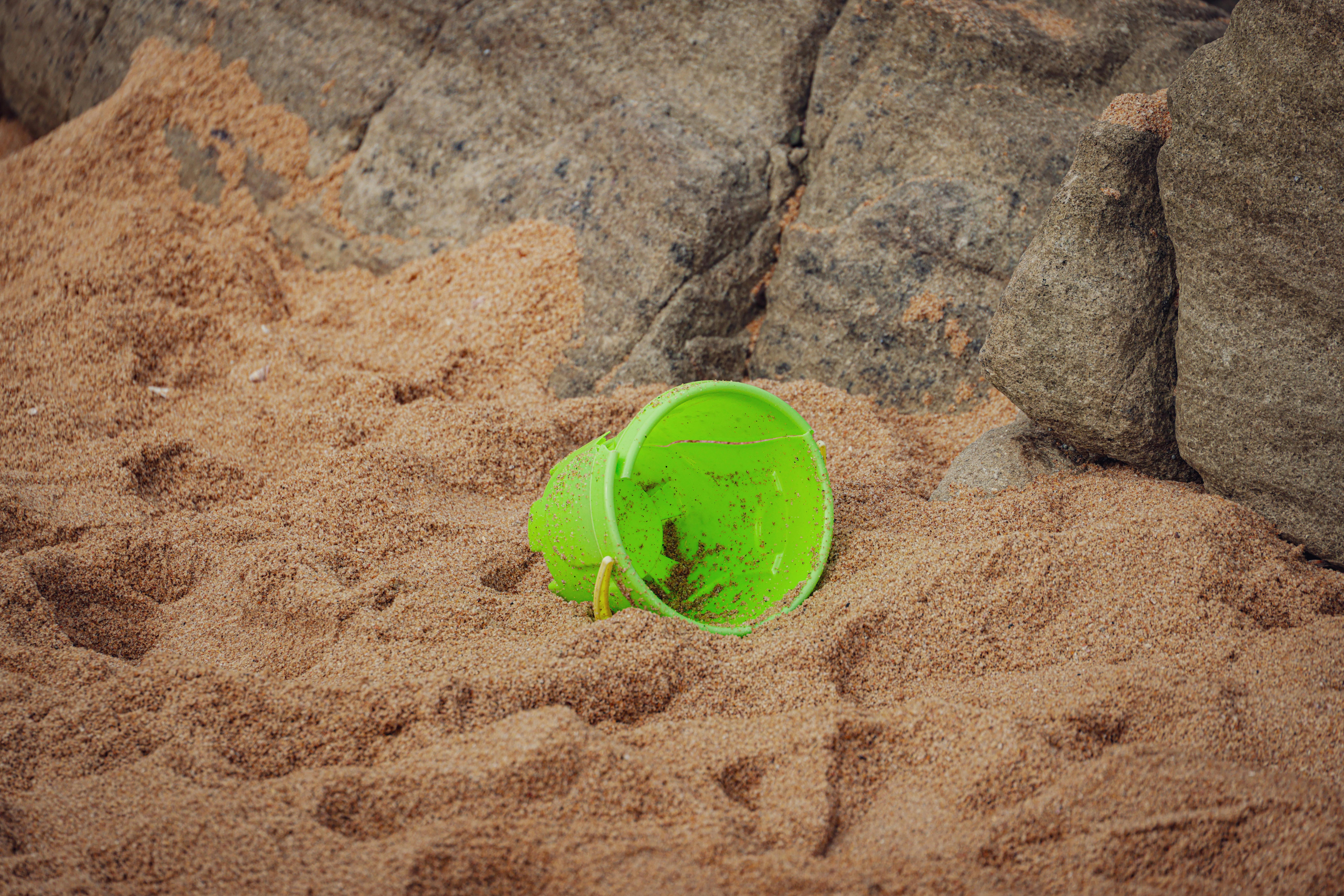 Empty plastic toy bucket tipped over in the sand